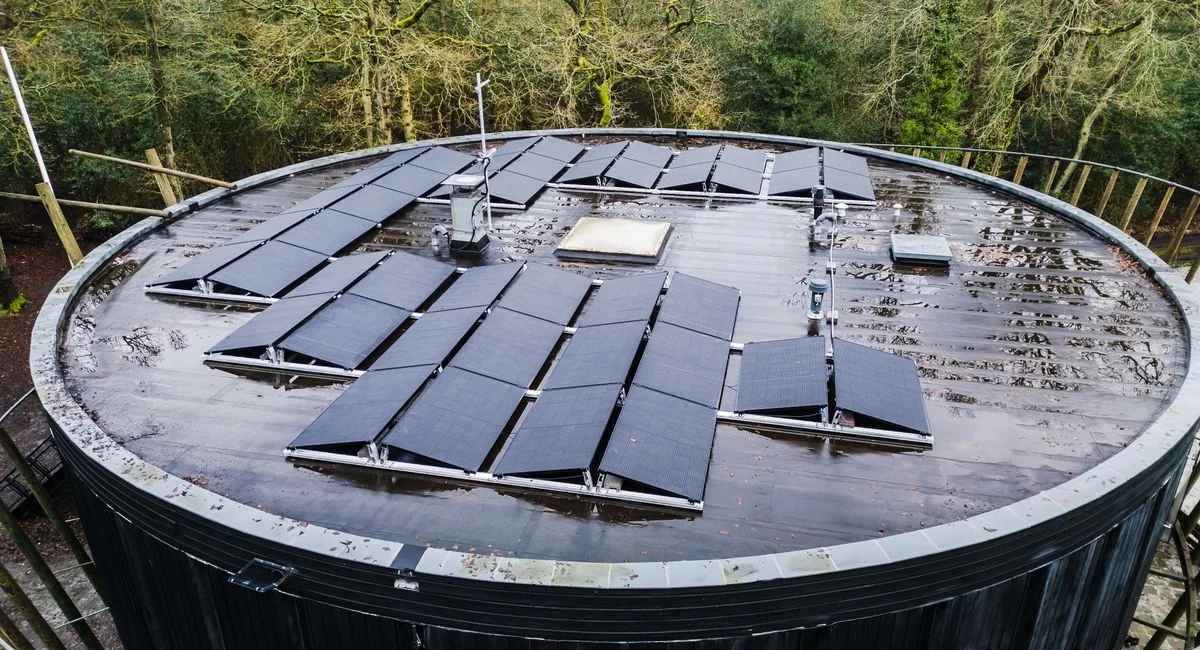 Aerial view of a round rooftop with solar panels surrounded by trees, promoting renewable energy.