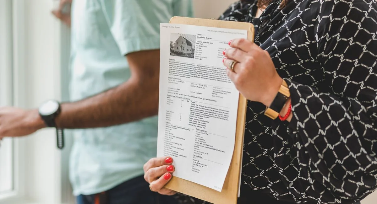 Real estate agent holding property documents on a clipboard in an office setting.