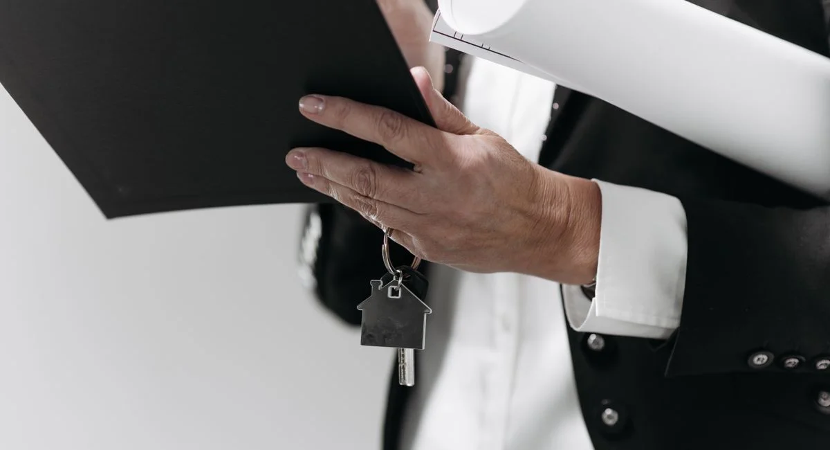 Close-up of a business professional holding a house key and architectural plans, symbolizing real estate.