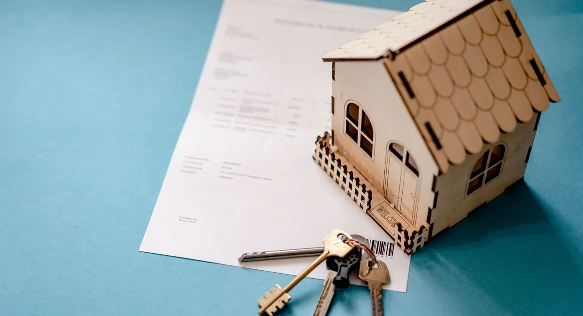 Miniature wooden house with keys and contract symbolizing real estate transactions.