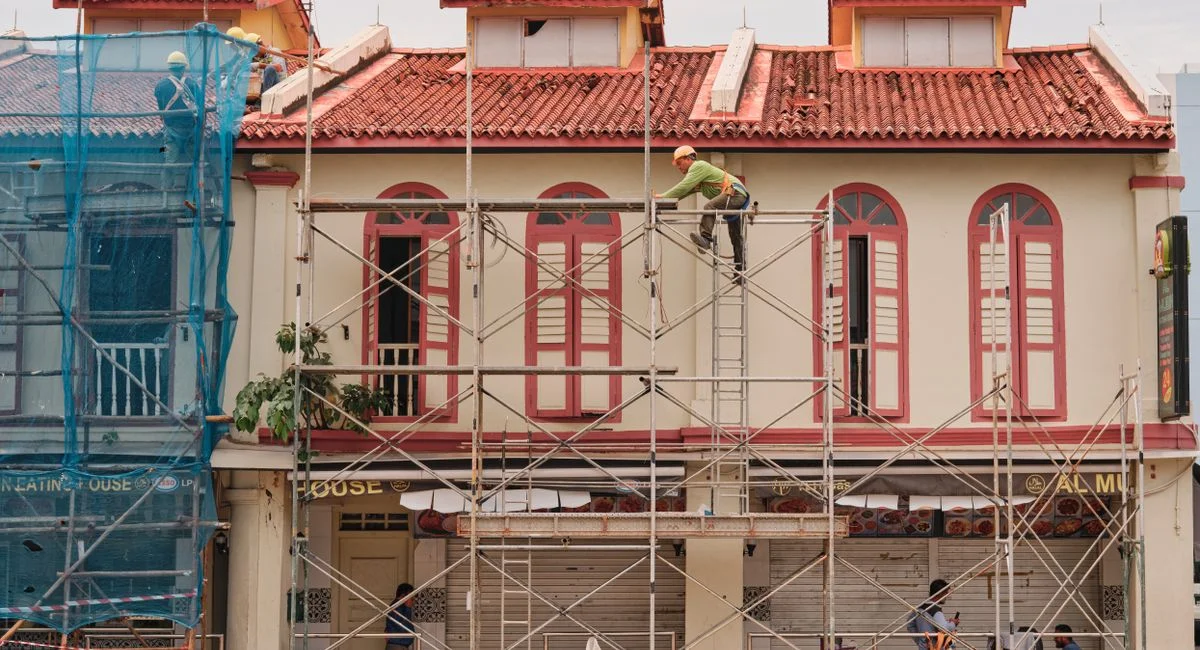 Workers on scaffolding renovating a historic building facade with red roof and tall windows.