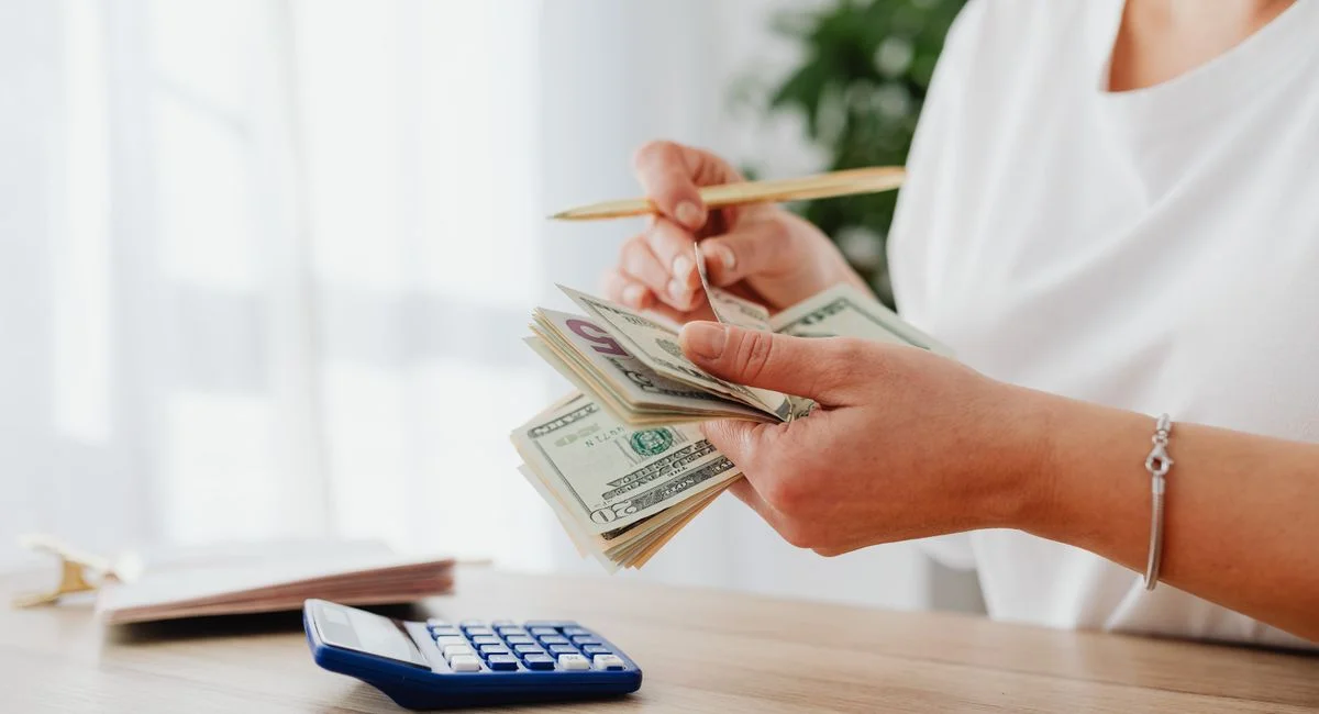 Close-up of a woman holding US dollars, calculating finances at home.