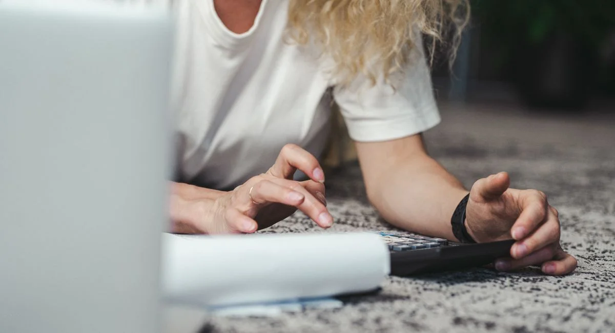 A woman engages in budget planning using a calculator on a comfortable carpeted floor.