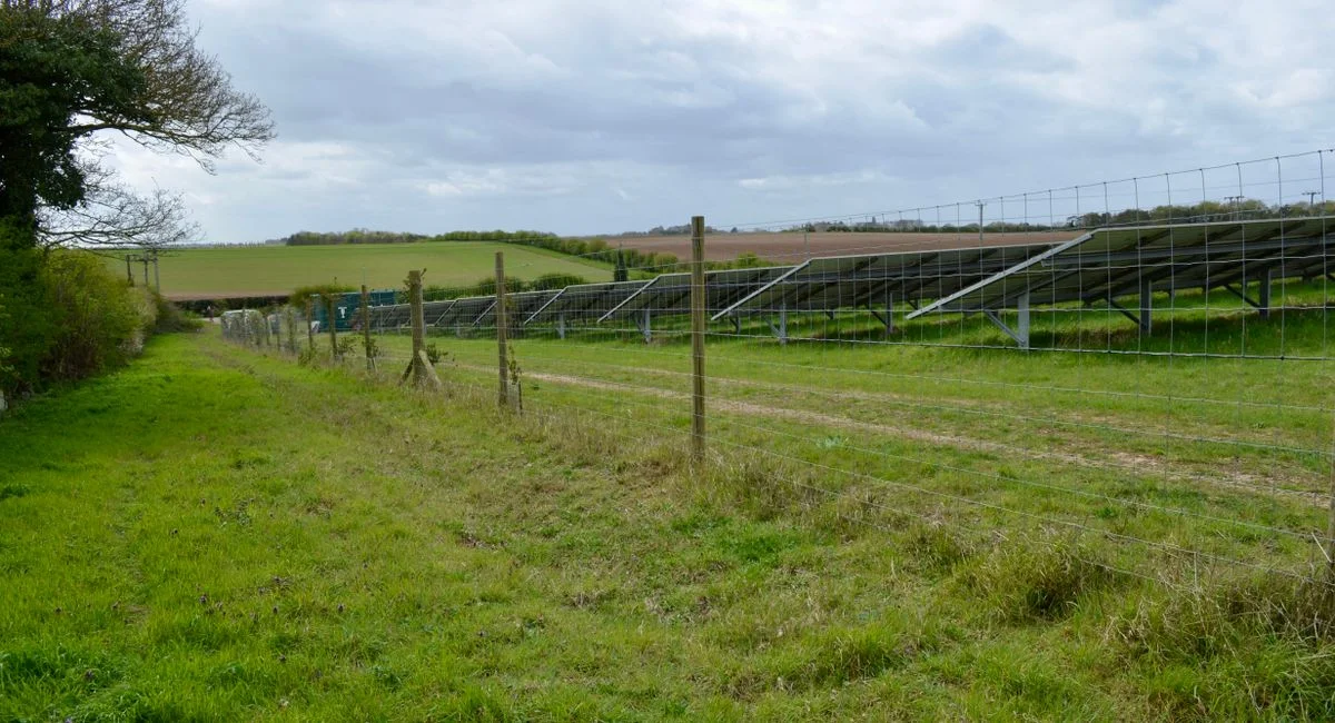 Solar panels installed in a rural field landscape under a cloudy sky.