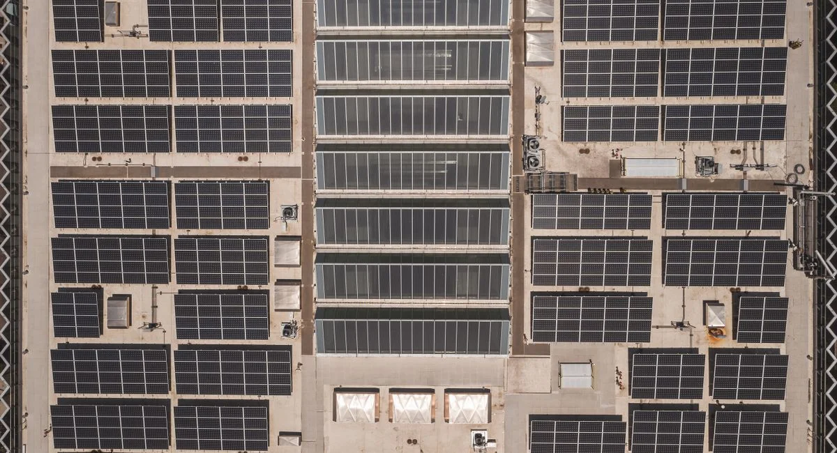 A high-angle drone shot capturing a grid of solar panels on a large industrial rooftop, showcasing renewable energy.