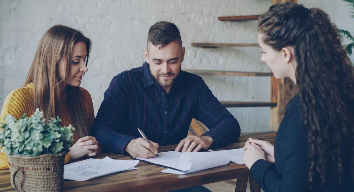 A young couple discussing paperwork with a real estate agent indoors.