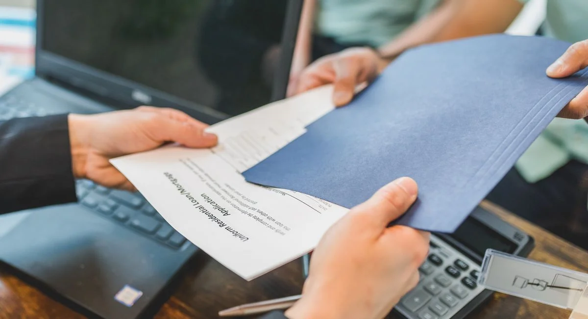 Close-up of hands exchanging real estate documents in an office setting.