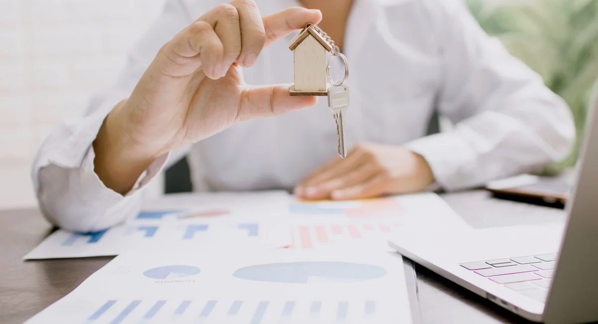 Real estate professional presenting a house model with keys, symbolizing property investment and ownership.