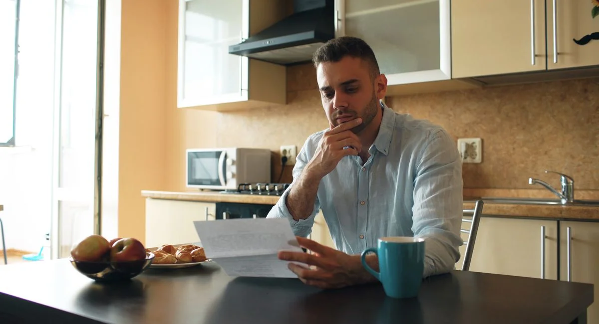 Thoughtful man reads a letter in a cozy kitchen setting with sunlight.