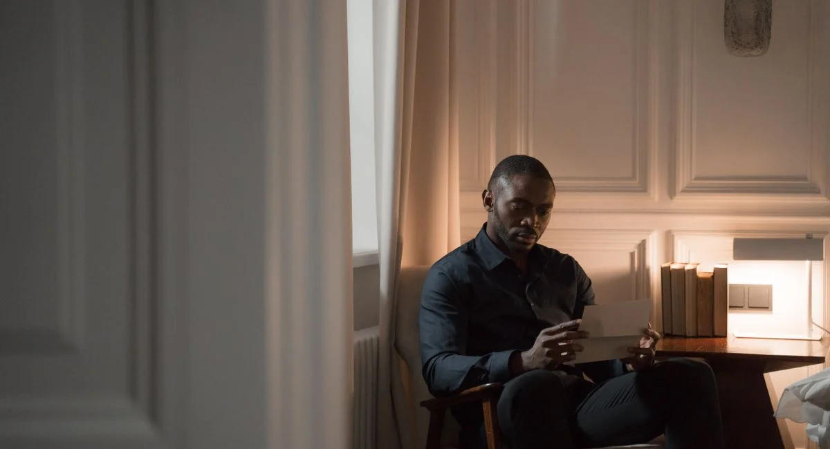 A thoughtful man reads a letter while sitting in a cozy room with soft lighting.