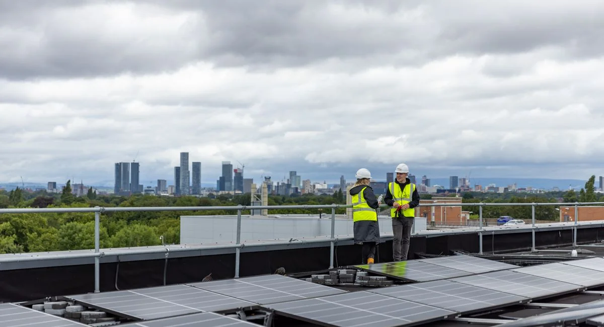 Two workers checking solar panels on a rooftop with a city skyline in the background.