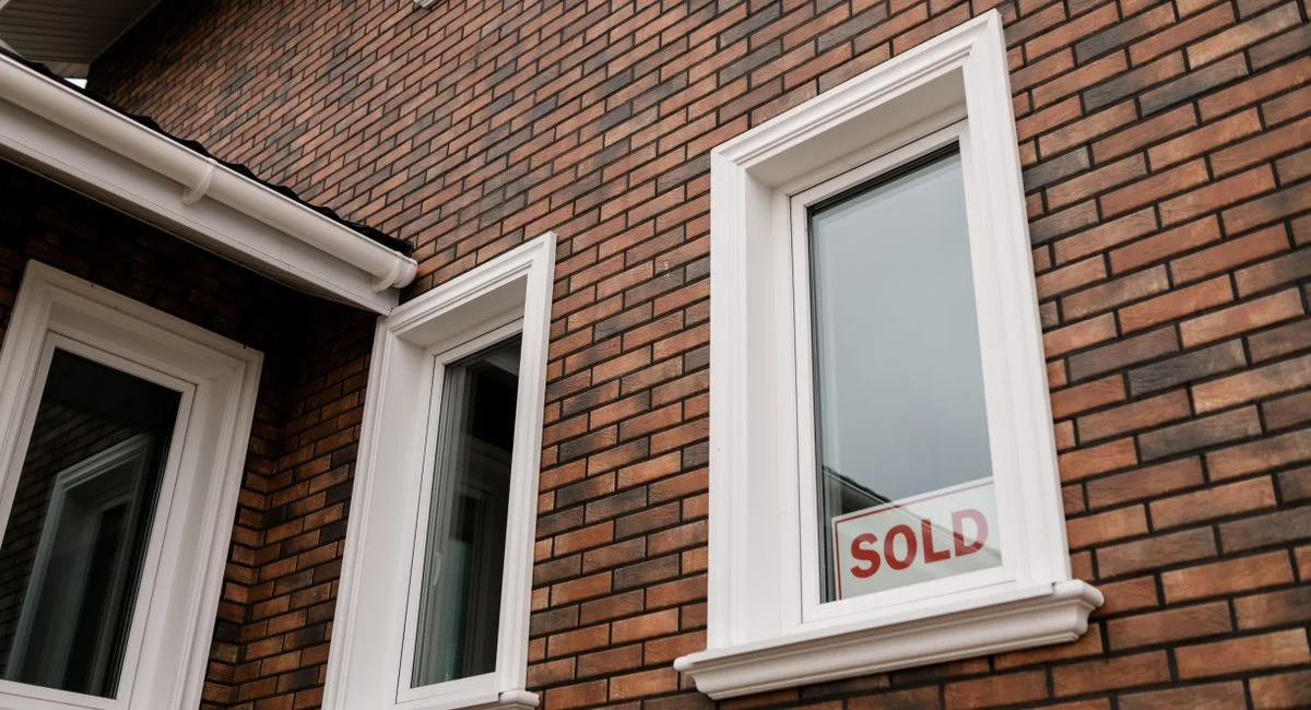 Close-up of a brick house with a 'Sold' sign in the window, showcasing real estate sales.